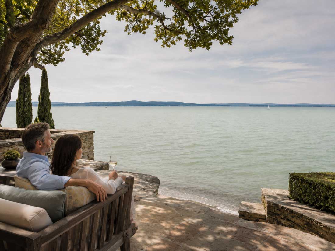 Hochwertige Terrasse am Balaton in Somogy mit sitzendem Paar, edlen Gartenmöbeln und ruhigem Blick auf den See