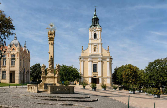 Stadtzentrum von Szekszárd im Komitat Tolna mit barocker Kirche und Dreifaltigkeitssäule unter blauem Himmel