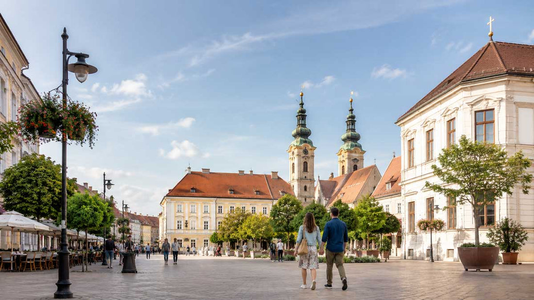 Historische Innenstadt von Székesfehérvár in Ungarn mit Spaziergängern, barocken Gebäuden und Kirchtürmen bei hellem Tageslicht im Querformat.